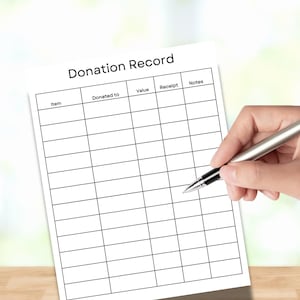 May include: A white sheet of paper with the words "Donation Record" at the top. The paper has a grid of blank boxes for filling in information. A hand holds a silver pen over the paper, ready to write.