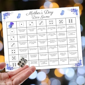 May include: Mother's Day Dice Game with prompts for sharing memories and stories about mothers. The game board is white with blue floral accents and dice illustrations. A hand is shown rolling a die.