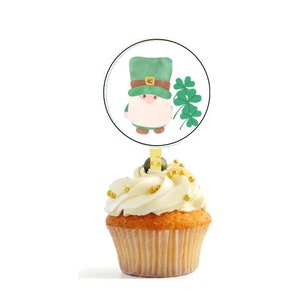 May include: A green leprechaun cupcake topper with a gold buckle on his hat and a shamrock. The topper is on a white cupcake with gold sprinkles.