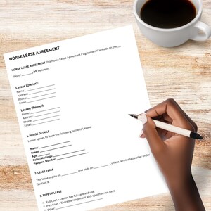 May include: A white sheet of paper with a "HORSE LEASE AGREEMENT" form is on a light wood surface. A hand holding a pen is writing on the form. A white coffee cup filled with dark liquid is in the upper right corner.