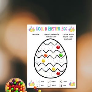 May include: A white game sheet with the text "ROLL A EASTER EGG" and an egg-shaped game board. Colorful candies are scattered around a clear bowl. The game instructions are: Roll a Die, Place a Candy on the matching color, and Be the first to fill your Easter Egg to win!