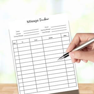 Peut inclure: Une feuille blanche intitulée "Mileage Tracker" avec du texte noir et des lignes de grille. La feuille comprend des champs pour les dates, le véhicule, le kilométrage et les détails. Une main tient un stylo.