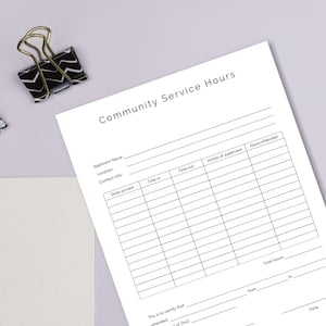 May include: A white Community Service Hours form with pre-printed fields for applicant information, time tracking, and supervisor initials. A black and white patterned binder clip rests near the form.