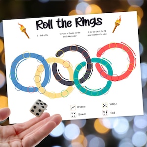 May include: A white game board with the text "Roll the Rings" and instructions. The board features five interlocking rings in blue, black, green, yellow, and red. A die is shown next to the board. The game is designed to help children learn colors.