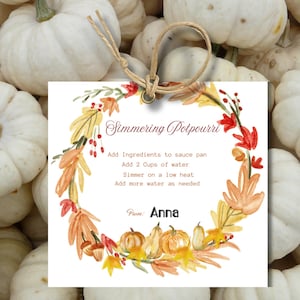 May include: A white tag with the text "Simmering Potpourri" and instructions, surrounded by a watercolor wreath of fall leaves and pumpkins. The tag is attached to a bundle of small white pumpkins with a twine string.