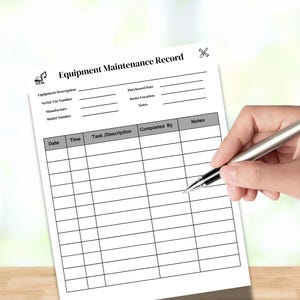 May include: A white Equipment Maintenance Record sheet with a hand holding a silver pen. The form includes fields for equipment description, serial number, and maintenance details. The text "Equipment Maintenance Record" is at the top.