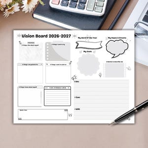 Puede incluir: Un Vision Board blanco para 2026-2027 con secciones para metas y autorreflexión. Incluye indicaciones como "Mi palabra del año" y "Mis esperanzas y sueños". Un bolígrafo descansa sobre la superficie.
