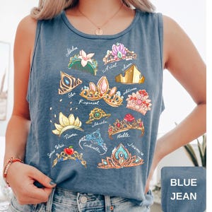 May include: Blue jean tank top featuring colorful illustrations of various princess crowns with names like Ariel, Belle, and Jasmine. The tank top is sleeveless and has a round neckline. The text "BLUE JEAN" is in a square box at the bottom right.