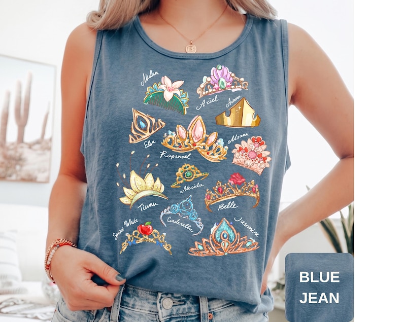 May include: Blue jean tank top featuring colorful illustrations of various princess crowns with names like Ariel, Belle, and Jasmine. The tank top is sleeveless and has a round neckline. The text "BLUE JEAN" is in a square box at the bottom right.