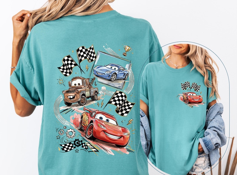 Puede incluir: Camiseta de color turquesa con un dise&ntilde;o de coches de carreras de dibujos animados, incluyendo un coche rojo, una gr&uacute;a marr&oacute;n y un coche azul, con banderas a cuadros y un trofeo. Una versi&oacute;n m&aacute;s peque&ntilde;a del dise&ntilde;o est&aacute; en el bolsillo.