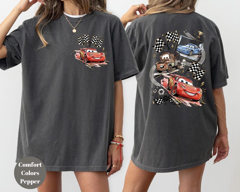Puede incluir: Camiseta gris oscuro con un coche de carreras de dibujos animados rojo y banderas a cuadros en la parte delantera. La parte trasera de la camiseta muestra tres coches de carreras de dibujos animados, banderas a cuadros y un trofeo. La camiseta est&aacute; hecha de un material suave y c&oacute;modo.