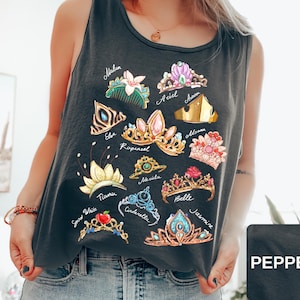May include: Dark gray tank top featuring colorful illustrations of various princess tiaras. Each tiara is labeled with a princess name, including Ariel, Belle, and Jasmine. The tank top is made of a soft material and is perfect for casual wear.