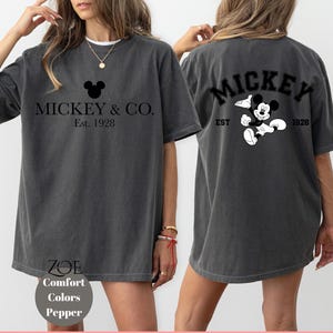 Puede incluir: Una camiseta gris de gran tama&ntilde;o con un gr&aacute;fico de Mickey Mouse negro y el texto "Mickey & Co. Est. 1928" en la parte delantera. La parte posterior de la camiseta tiene un gr&aacute;fico de Mickey Mouse negro y el texto "Mickey Est. 1928".