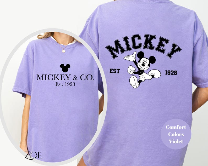 Puede incluir: Una camiseta morada con un gr&aacute;fico de Mickey Mouse negro y el texto "Mickey & Co. Est. 1928" en la parte delantera. La parte posterior de la camiseta tiene un gr&aacute;fico de Mickey Mouse m&aacute;s grande con el texto "Mickey Est. 1928".