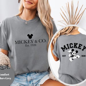 Puede incluir: Camiseta gris con un gr&aacute;fico negro de Mickey Mouse y el texto "Mickey & Co. Est. 1928" en la parte delantera. La parte posterior de la camiseta tiene un gr&aacute;fico negro de Mickey Mouse con el texto "Mickey Est. 1928".