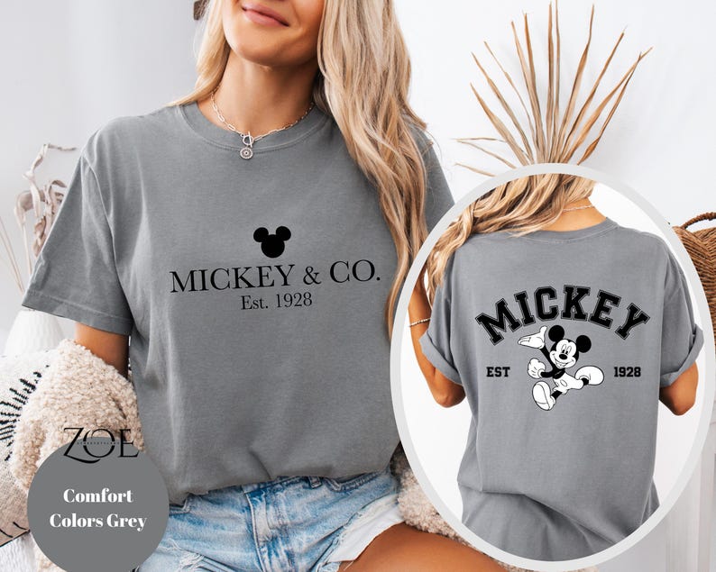 Puede incluir: Camiseta gris con un gr&aacute;fico negro de Mickey Mouse y el texto "Mickey & Co. Est. 1928" en la parte delantera. La parte posterior de la camiseta tiene un gr&aacute;fico negro de Mickey Mouse con el texto "Mickey Est. 1928".