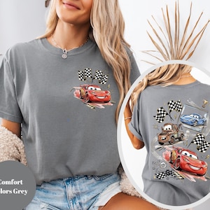 Puede incluir: Camiseta gris con un gr&aacute;fico de Rayo McQueen de la pel&iacute;cula Cars, con banderas a cuadros. La parte posterior de la camiseta muestra a Rayo McQueen, Mate y un coche azul. El texto "Comfort Colors Grey" es visible.