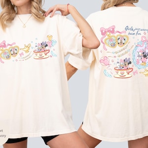 May include: Ivory t-shirt with a colourful graphic of Minnie and Daisy Mouse in teacups and heart-shaped lockets. The back of the shirt has the text "Girls just wanna have fun" with additional graphics. The shirt is a comfort fit.