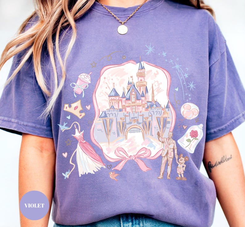 May include: A violet-colored t-shirt featuring a whimsical illustration of a fairytale castle, a dress, a crown, and other themed elements. The design includes a bow and a couple with a child. The word "VIOLET" is printed on the bottom left.