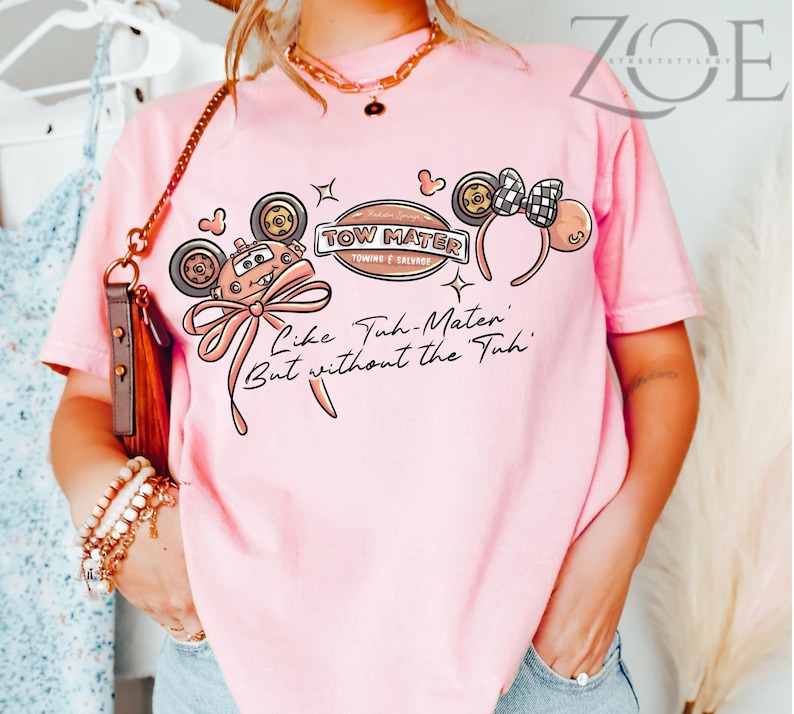 Może przedstawiać: Jasnor&oacute;żowa koszulka z kresk&oacute;wkowym wzorem. Wz&oacute;r zawiera tekst "TOW MATER" i "Like Tuh-Mater But without the Tuh", samoch&oacute;d z kresk&oacute;wek, uszy Myszki Miki i kokardę.