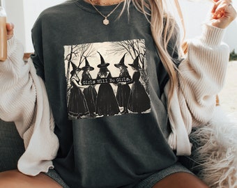 May include: Dark gray sweatshirt featuring a black and white graphic of five witches in pointed hats and long dresses. The text "Girls Will Be Girls" is printed on the graphic. The sweatshirt has a relaxed fit.