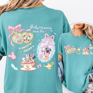 May include: Teal t-shirt with a cartoon design featuring Minnie Mouse, Daisy Duck, and other Disney characters. The shirt includes the text "Girls just wanna have fun" and decorative elements like bows, teacups, and a magic lamp.