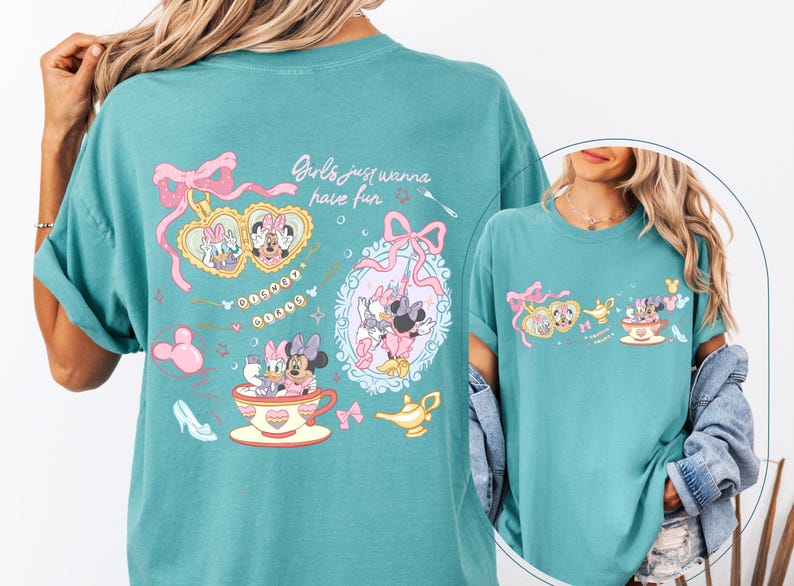 May include: Teal t-shirt with a cartoon design featuring Minnie Mouse, Daisy Duck, and other Disney characters. The shirt includes the text "Girls just wanna have fun" and decorative elements like bows, teacups, and a magic lamp.