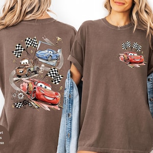 Puede incluir: Camiseta color espresso con un gr&aacute;fico de coches de carreras animados, incluido un coche rojo con una cara sonriente y banderas a cuadros. La parte posterior de la camiseta tiene un dise&ntilde;o m&aacute;s grande con m&uacute;ltiples coches y elementos de carreras.