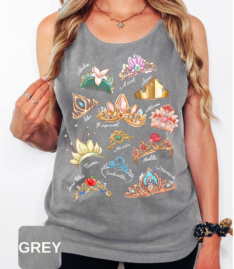 May include: Gray tank top featuring colorful illustrations of various princess crowns. Each crown is labeled with a princess name, including Ariel, Belle, and Cinderella. The shirt has a casual, relaxed fit.