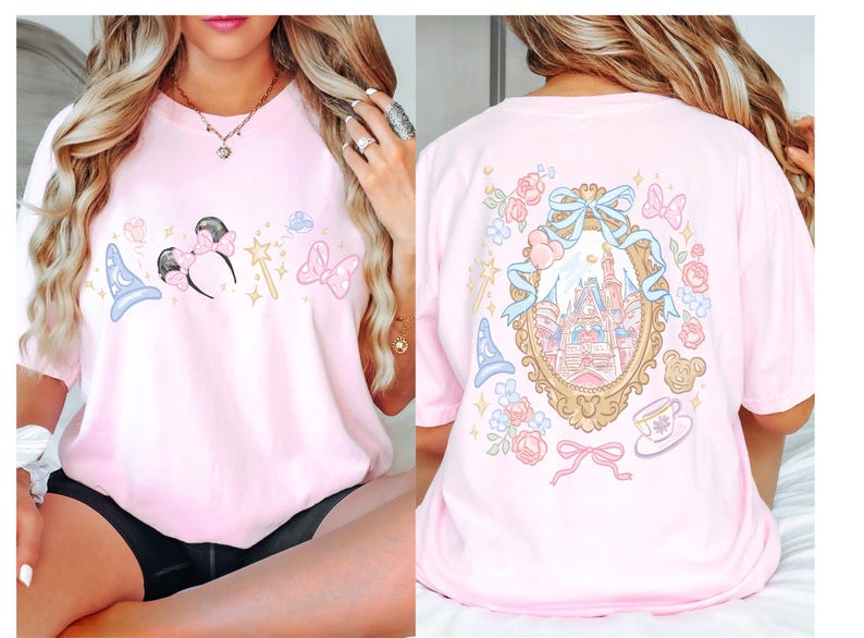May include: A light pink t-shirt featuring a front design of a blue wizard hat, Minnie Mouse ears, a magic wand, and a pink bow. The back of the shirt displays a castle scene within a gold frame, surrounded by floral and bow accents.