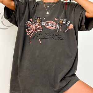 Może przedstawiać: Ciemnoszara koszulka z nadrukiem przedstawiającym samoch&oacute;d, kokardę i opaskę na głowę. Tekst na koszulce brzmi "Tow Mater" i "Like Tow Mater But without the Tuh". Projekt zawiera r&oacute;żowe i czarne akcenty.