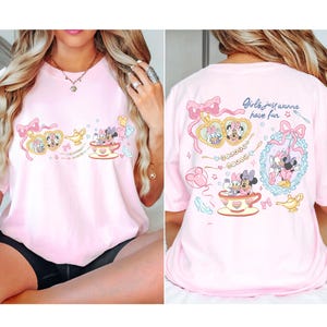 May include: A pale pink t-shirt with a cartoon design featuring Minnie and Daisy Mouse. The front design includes teacups, bows, and a magic lamp. The back of the shirt has the text "Girls just wanna have fun."