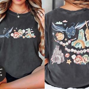 May include: Dark gray t-shirt with colorful cartoon graphics on the front and back. The front features characters and elements from popular video games and movies. The back has the words "EPIC UNIVERSE" and more cartoon graphics.