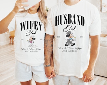 May include: White t-shirts with black text and a cartoon image of Mickey Mouse and Minnie Mouse dressed as a bride and groom. The text on the shirts reads "Wifey Club" and "Husband Club" with the year "2025" and the text "Mr. & Mrs. Hayes JUST MARRIED".