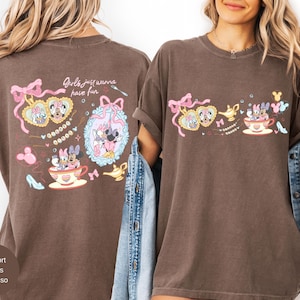 May include: Espresso-coloured t-shirt with a playful design of Minnie and Daisy Duck. The graphic includes a teacup, high heels, and the phrase "Girls just wanna have fun." The design is in shades of pink, yellow, and blue.