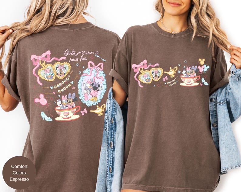 May include: Espresso-coloured t-shirt with a playful design of Minnie and Daisy Duck. The graphic includes a teacup, high heels, and the phrase "Girls just wanna have fun." The design is in shades of pink, yellow, and blue.