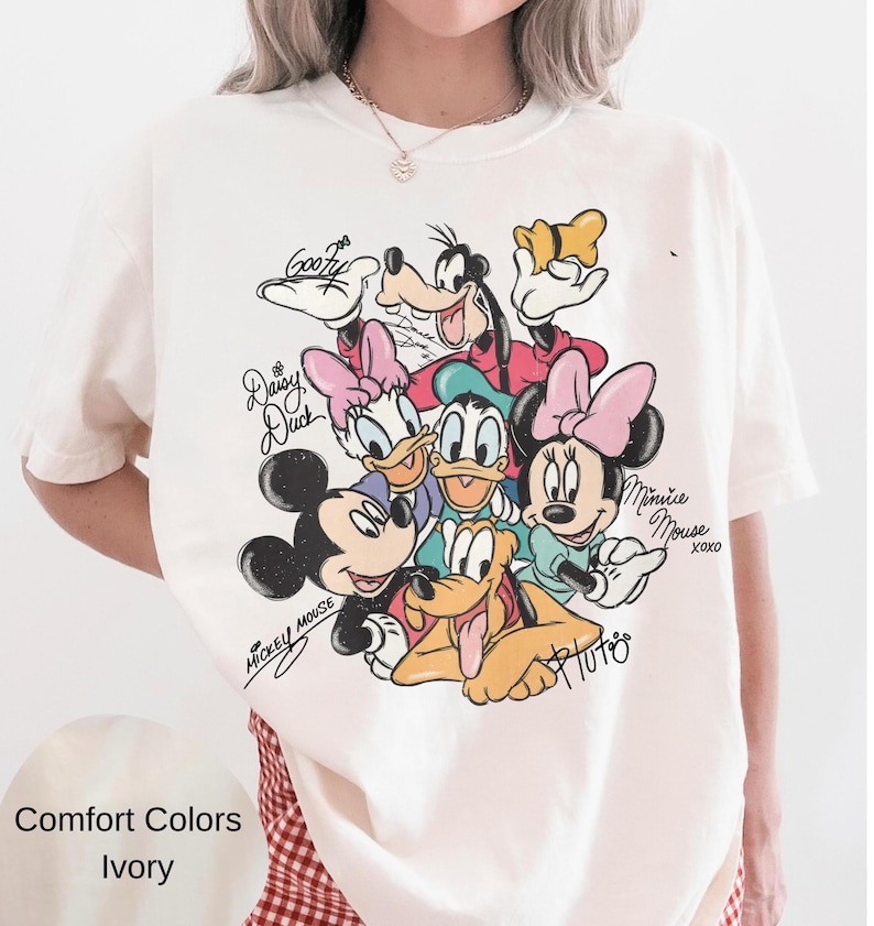 以下が含まれることがあります： アイボリー色のComfort Colors Tシャツ。ミッキーマウス、ミニーマウス、ドナルドダック、デイジーダック、グーフィー、プルートなど、ディズニーキャラクターのカラフルなグラフィックが特徴です。「Mickey Mouse」と「Minnie Mouse XOXO」の文字入り。