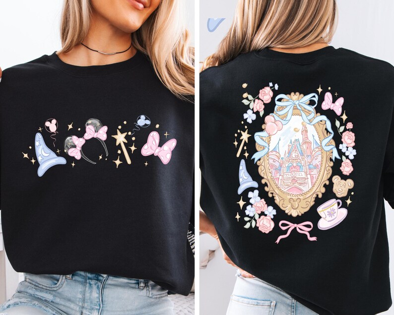 May include: Black sweatshirt featuring a whimsical design with a light blue wizard hat, pink bow, and a wand on the front. The back showcases a castle in a gold frame surrounded by flowers, bows, and a teacup.