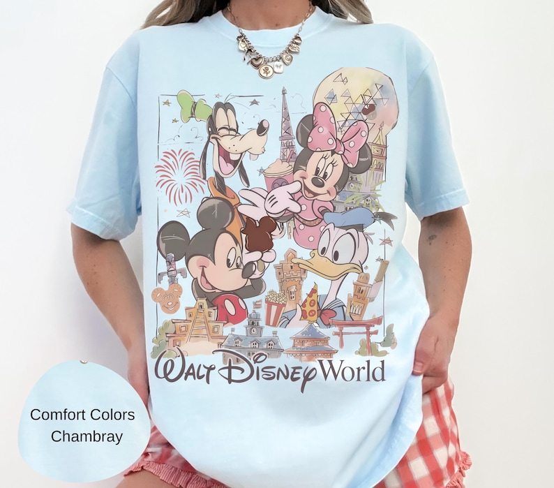 May include: A light blue t-shirt featuring a graphic print of Mickey Mouse, Minnie Mouse, Goofy, and Donald Duck in front of Walt Disney World landmarks. The text Walt Disney World is printed at the bottom of the graphic in a dark brown script font.