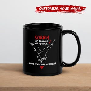 May include: Black ceramic mug with a white graphic of two hands clasped together. The mug has the text "Sorry, No Refunds or Returns" and "You're Stuck With Me Forever". The top of the mug has the text "Customize Your Name".