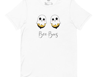 May include: White t-shirt featuring a playful design of two cartoon bees dressed as ghosts. The bees have white ghost-like bodies with smiling faces and are perched on yellow and black bee bodies. The words "Boo Bees" are written below.