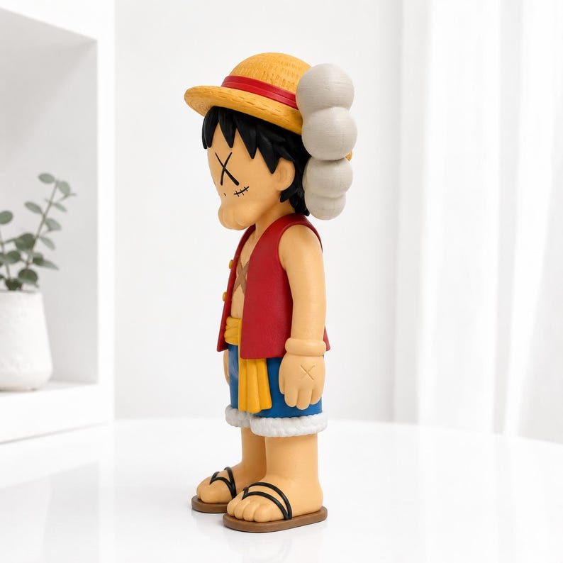 May include: A stylized collectible figure of a character wearing a yellow straw hat with a red band, a red vest, a yellow sash, and blue shorts. The figure has black hair, tan skin, and X-shaped markings over the eyes, standing on a flat base.