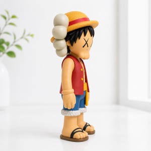 May include: A collectible vinyl figure of a character wearing a yellow straw hat with a red band, a red vest, blue shorts with a white frayed hem, and black sandals. The figure features black hair, tan skin, and X-shaped marks over the eyes.