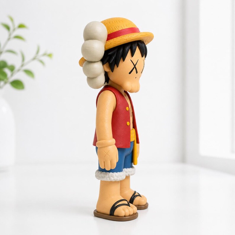 May include: A collectible vinyl figure of a character wearing a yellow straw hat with a red band, a red vest, blue shorts with a white frayed hem, and black sandals. The figure features black hair, tan skin, and X-shaped marks over the eyes.