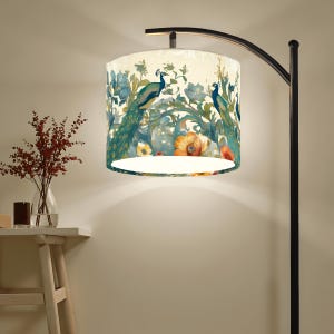 May include: A floor lamp with a black metal frame and a drum shade. The shade features a cream background with a peacock and floral design in shades of teal, blue, orange, and yellow. The lamp is in a well-lit room.