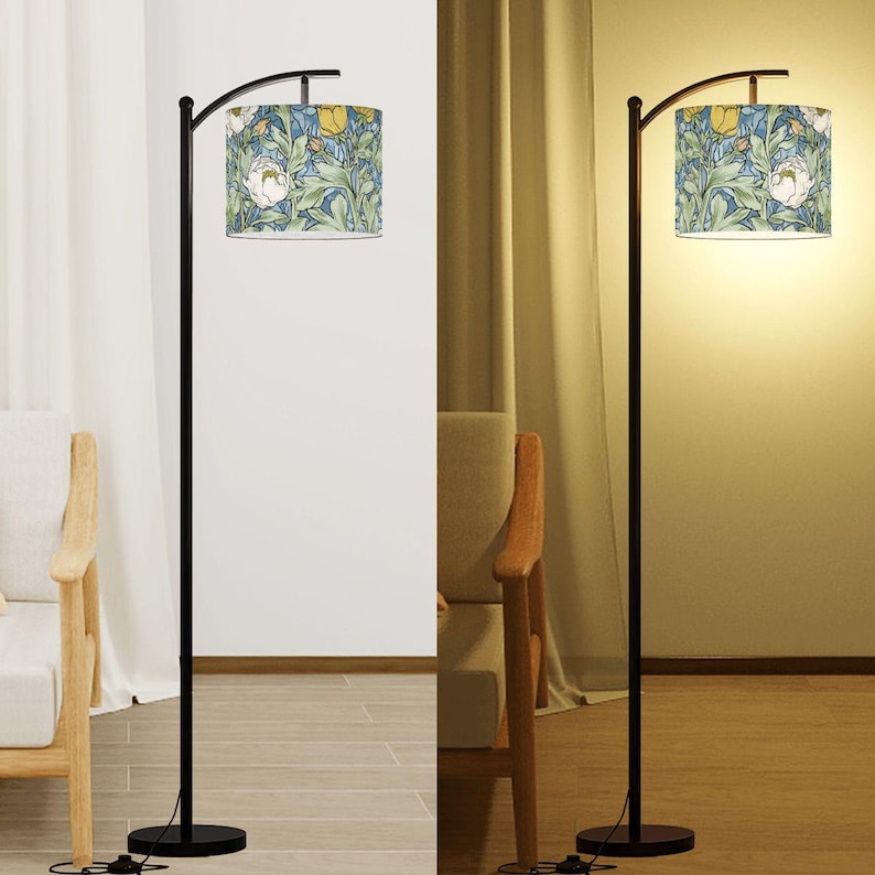 May include: A black floor lamp with a curved arm supporting a cylindrical lampshade. The lampshade features a floral pattern with white, yellow, and blue flowers on a light blue background. The lamp is on a round black base.