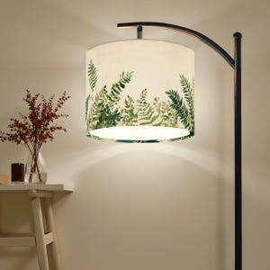 May include: A black arc floor lamp with a cream-colored lampshade. The lampshade features a green fern leaf pattern. A small table with a vase of red flowers and a candle sits to the left of the lamp.