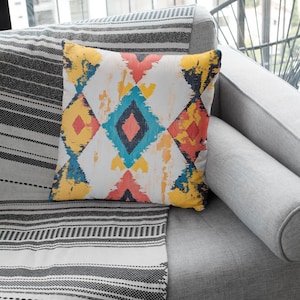 May include: A gray couch with a black and white striped throw blanket and a colorful geometric patterned pillow. The pillow has a diamond pattern with shades of yellow, blue, red, and black.