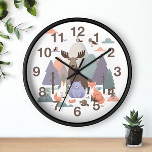 Può includere: Un orologio da parete rotondo con cornice nera. Il quadrante presenta una scena della foresta con un alce, un orso, una volpe e altri animali. I numeri sono in marrone. Le lancette dell'orologio sono nere.