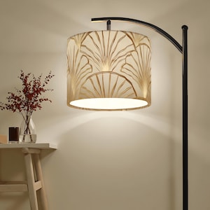 May include: A floor lamp with a black metal frame and a cream-colored lampshade. The lampshade features a gold fan-shaped design. A small table with a vase of red flowers is to the left of the lamp.